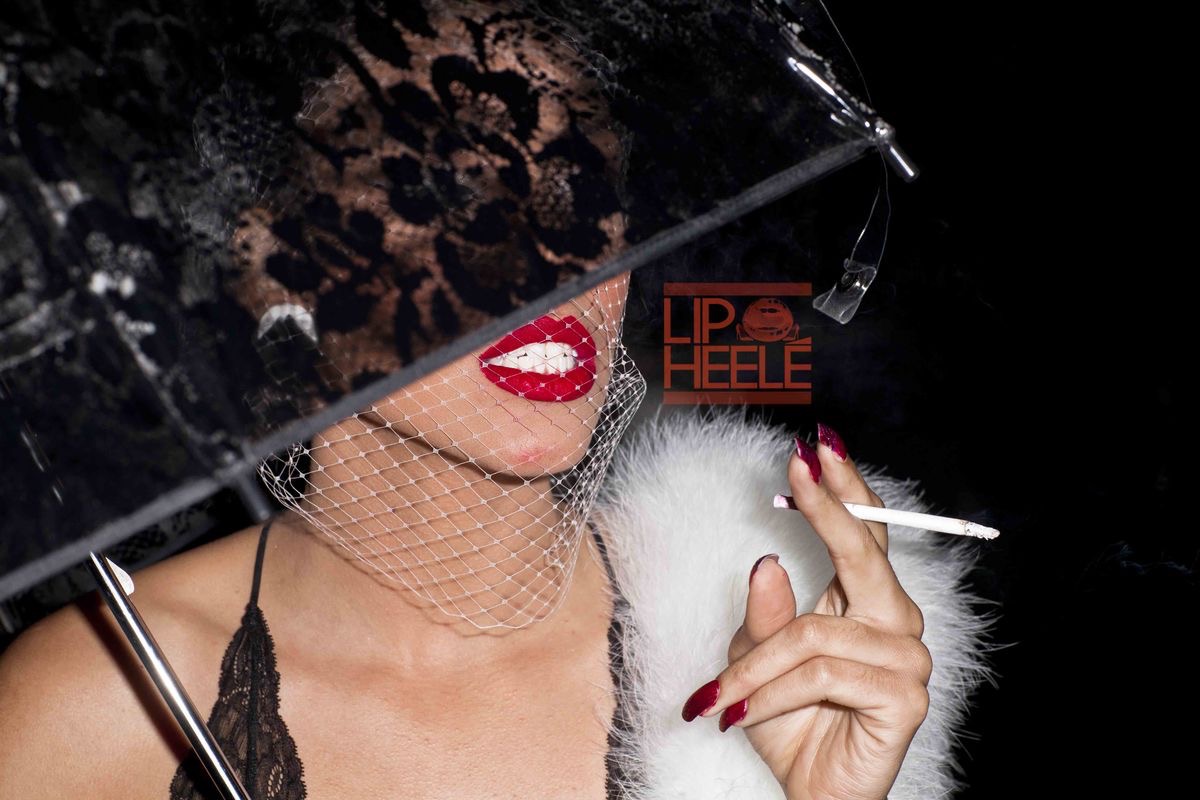 Close-up portrait with red lipstick, black lace veil, and white feather accents